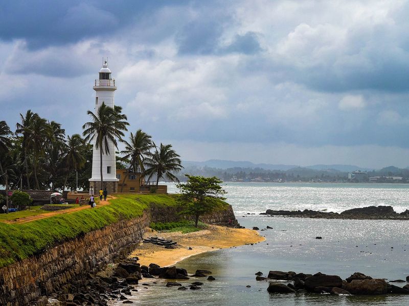 Galle Fort is one of the best of Sri Lanka's historical places. This image shows a tall white lighthouse on the waterfront against a grey sky.